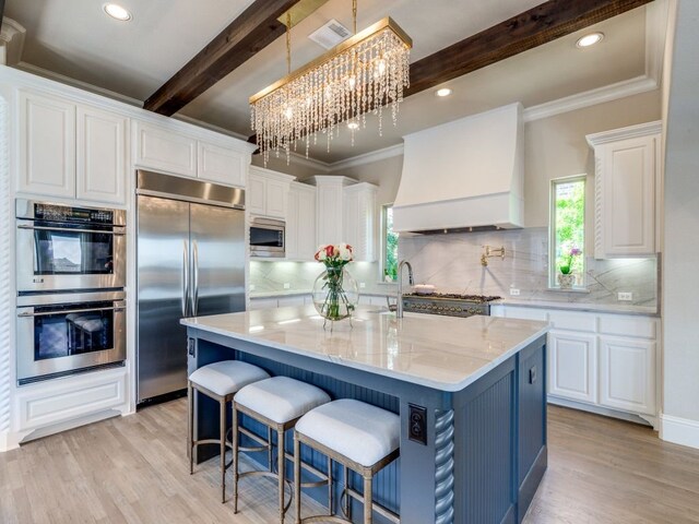 kitchen featuring beam ceiling, built in appliances, ornamental molding, light wood-style flooring, and premium range hood