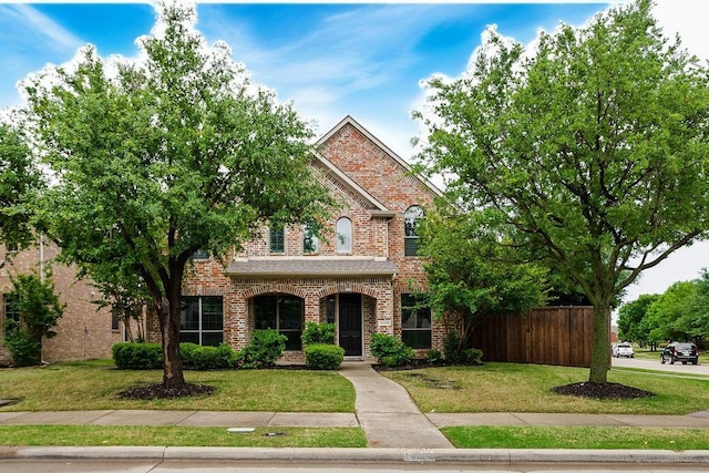 traditional-style home with a front lawn, brick siding, and fence