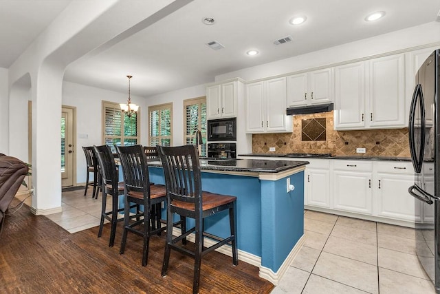 kitchen featuring black appliances, a kitchen bar, visible vents, and dark countertops
