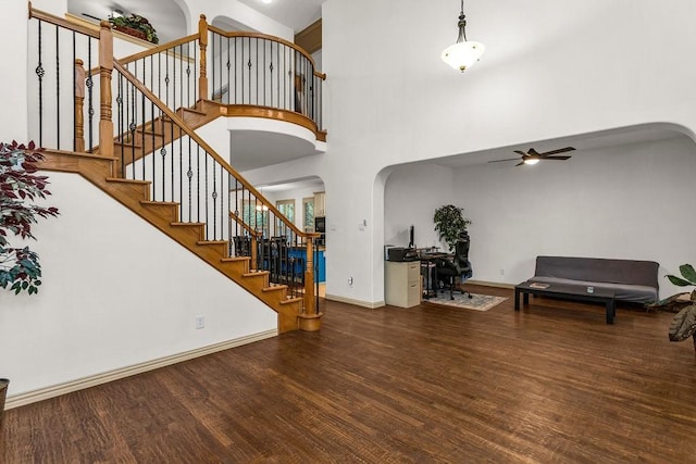 foyer entrance featuring arched walkways, wood finished floors, baseboards, a ceiling fan, and a towering ceiling
