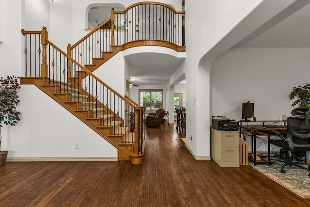 entryway with wood finished floors, arched walkways, stairs, baseboards, and a high ceiling