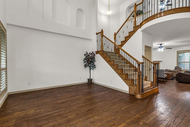 interior space with wood finished floors, a ceiling fan, baseboards, and a high ceiling
