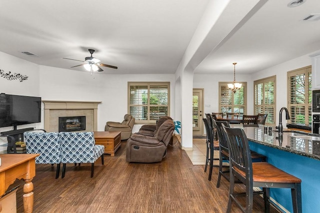 living area featuring ceiling fan with notable chandelier, visible vents, wood finished floors, and a high end fireplace