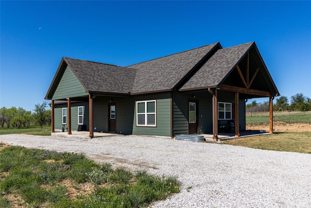 view of front of home featuring a porch, gravel driveway, and roof with shingles