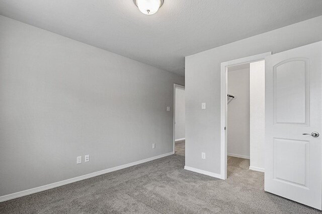 unfurnished bedroom with baseboards, carpet flooring, a closet, and a walk in closet