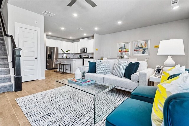 living area featuring ceiling fan, visible vents, stairs, and light wood finished floors