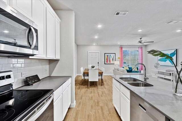 kitchen with stainless steel appliances, visible vents, a sink, decorative backsplash, and white cabinetry