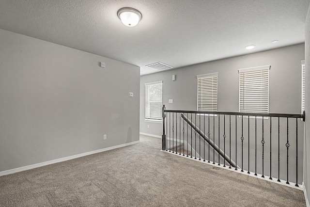 spare room featuring baseboards, visible vents, carpet floors, and a textured ceiling