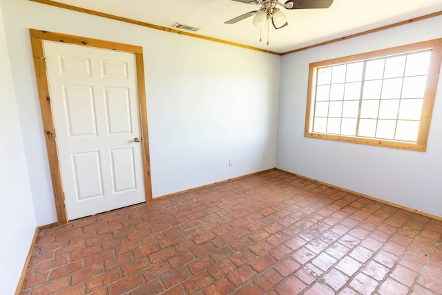 spare room featuring crown molding, brick floor, ceiling fan, baseboards, and visible vents