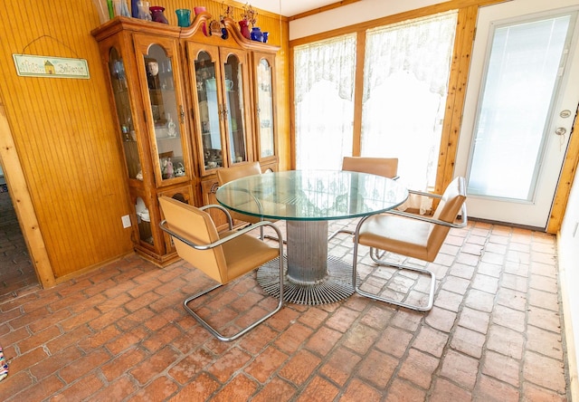 dining space featuring brick floor, wooden walls, and a healthy amount of sunlight