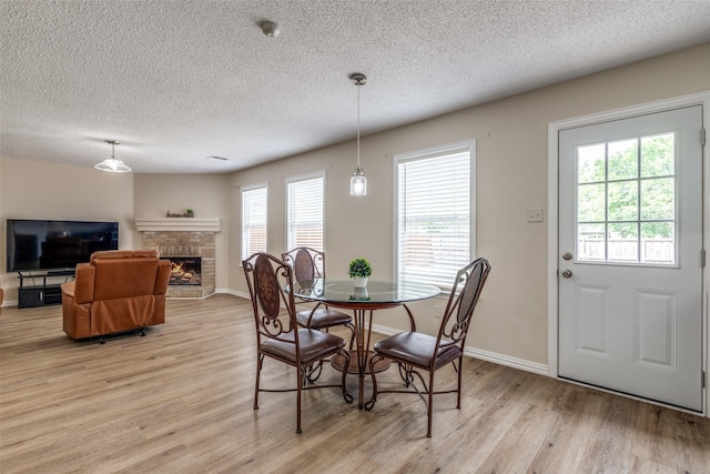 4504 Courtside Dr, Mckinney, TX 75070 - dining room featuring light wood-type flooring, a textured ceiling, a stone fireplace, and baseboards