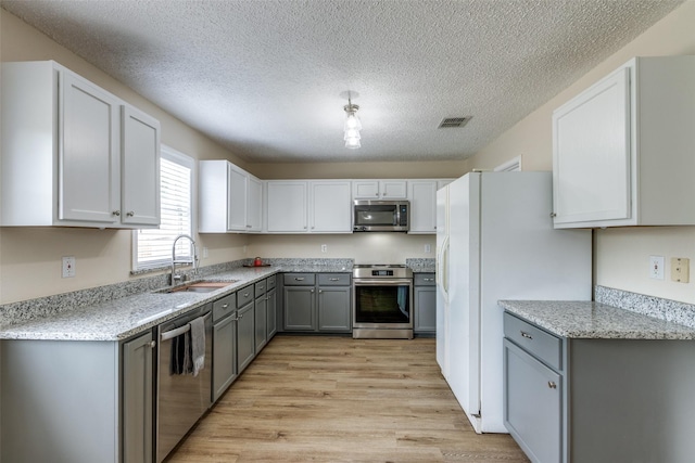 4504 Courtside Dr, Mckinney, TX 75070 - kitchen with stainless steel appliances, a sink, gray cabinets, light wood-style floors, and a textured ceiling
