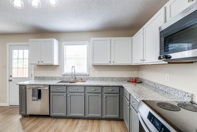 4504 Courtside Dr, Mckinney, TX 75070 - kitchen with appliances with stainless steel finishes, a sink, gray cabinets, light wood finished floors, and a textured ceiling