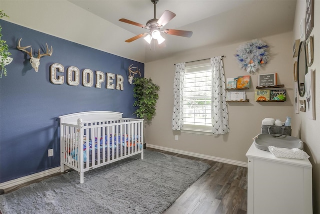 bedroom with baseboards, a ceiling fan, wood finished floors, and a nursery area