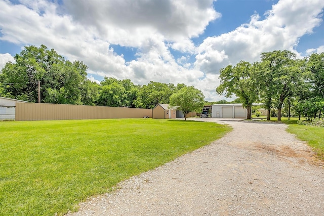 view of yard with a garage, driveway, fence, and an outdoor structure