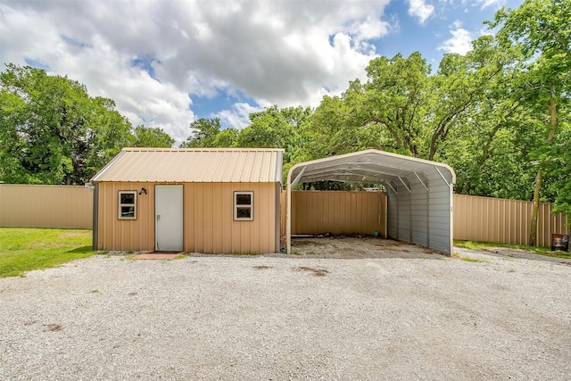 view of outbuilding featuring an outdoor structure, gravel driveway, a carport, and fence