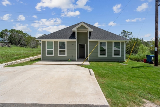 view of front facade with a shingled roof, driveway, and a front yard