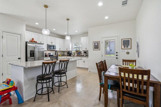 kitchen with finished concrete floors, appliances with stainless steel finishes, a center island with sink, white cabinetry, and visible vents