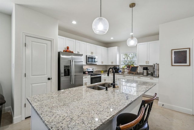 kitchen with a sink, an island with sink, white cabinetry, appliances with stainless steel finishes, and light stone countertops