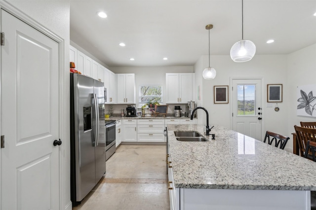 kitchen featuring a sink, appliances with stainless steel finishes, a center island with sink, white cabinetry, and light stone countertops