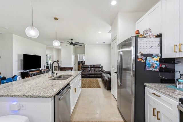 kitchen featuring white cabinets, a sink, open floor plan, light stone countertops, and appliances with stainless steel finishes
