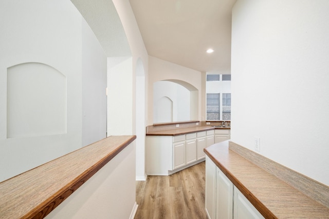 corridor with light wood-style flooring, baseboards, a sink, and recessed lighting