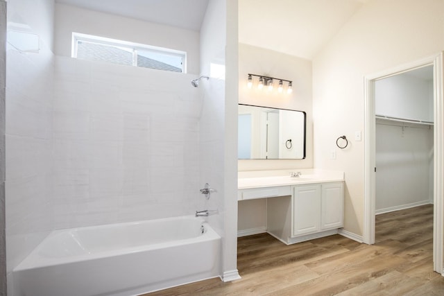 bathroom featuring lofted ceiling, a spacious closet, wood finished floors, vanity, and shower / bathing tub combination