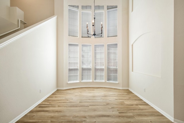 interior space featuring wood finished floors, a towering ceiling, baseboards, and a notable chandelier