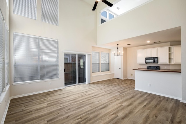 unfurnished living room featuring light wood-style flooring, a high ceiling, baseboards, and ceiling fan with notable chandelier