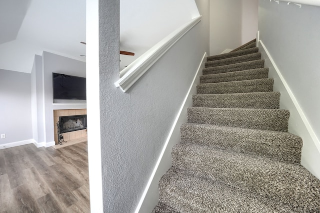 stairway featuring a tile fireplace, a ceiling fan, wood finished floors, and baseboards