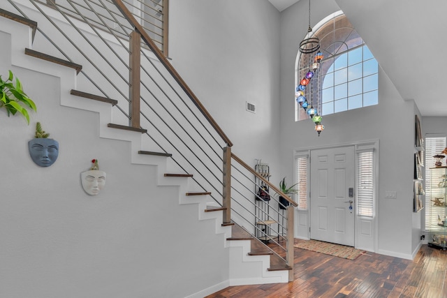 foyer with stairway, a towering ceiling, visible vents, wood-type flooring, and baseboards