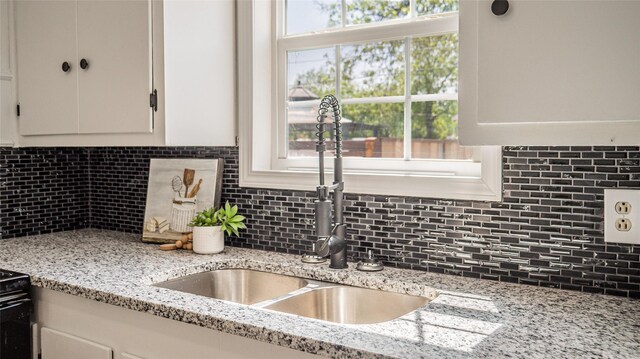 kitchen featuring white cabinets, backsplash, light stone countertops, and a sink