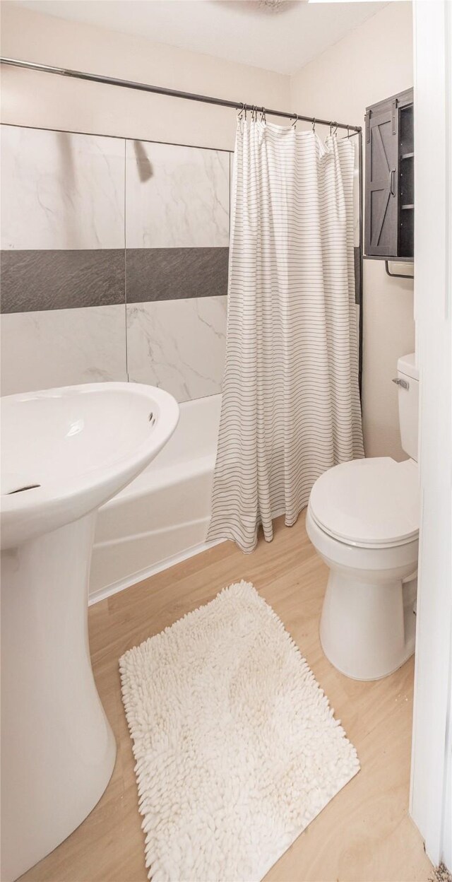 bathroom with shower / bath combination with curtain, wood finished floors, and toilet