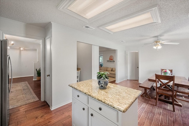 kitchen with a center island, a textured ceiling, visible vents, freestanding refrigerator, and white cabinetry