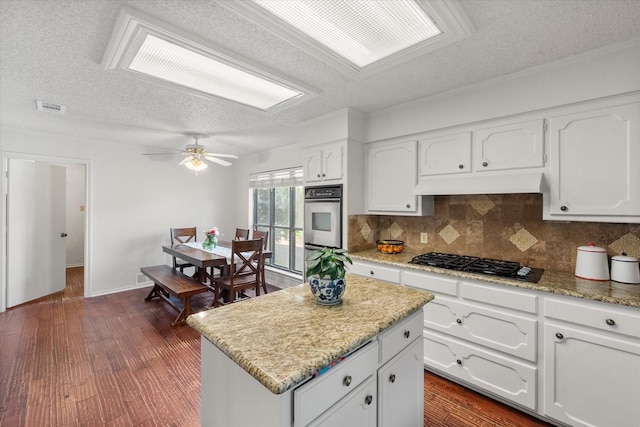 kitchen featuring tasteful backsplash, a textured ceiling, white cabinetry, under cabinet range hood, and black gas cooktop
