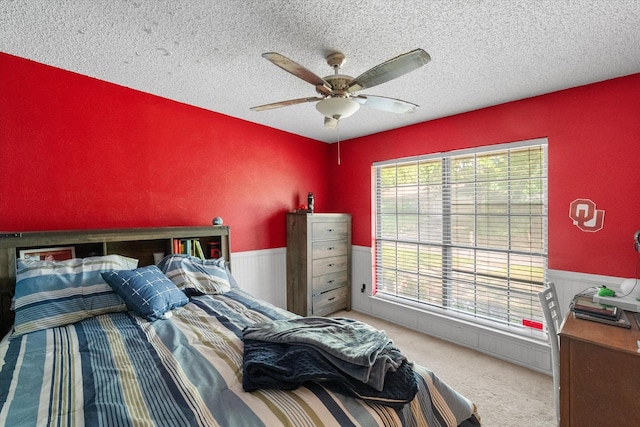 carpeted bedroom featuring a textured ceiling, a ceiling fan, and wainscoting