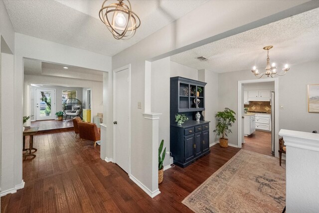 hallway with dark wood-style floors, a textured ceiling, and a notable chandelier