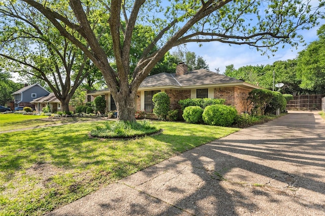 view of front of house with a chimney, driveway, fence, a front yard, and brick siding