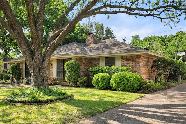 ranch-style home featuring brick siding, roof with shingles, a chimney, and a front lawn