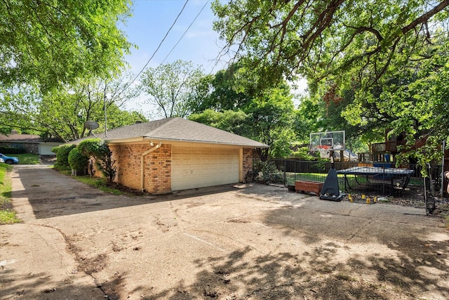 view of side of home with an outbuilding, roof with shingles, fence, brick siding, and a garage