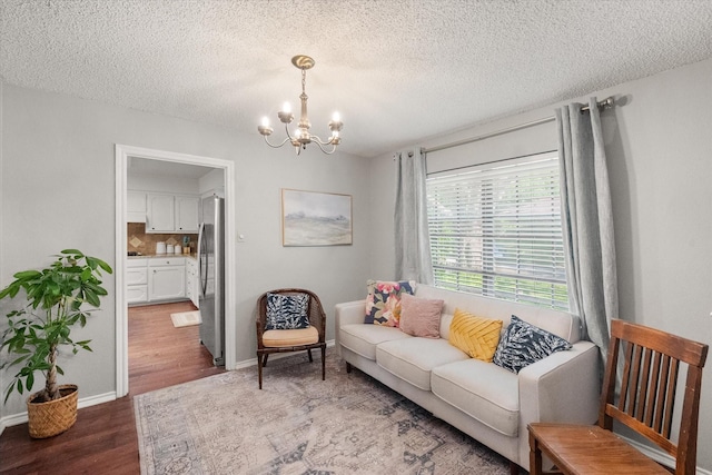 living area with baseboards, wood finished floors, a textured ceiling, and a notable chandelier