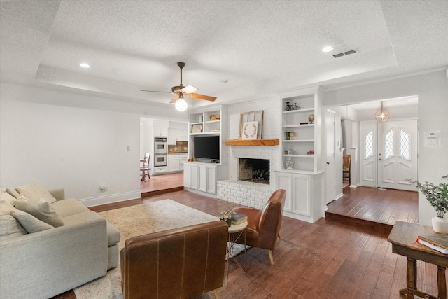 living room featuring a tray ceiling, a textured ceiling, visible vents, and hardwood / wood-style flooring