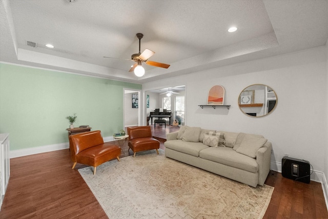 living area with a tray ceiling, visible vents, and ceiling fan