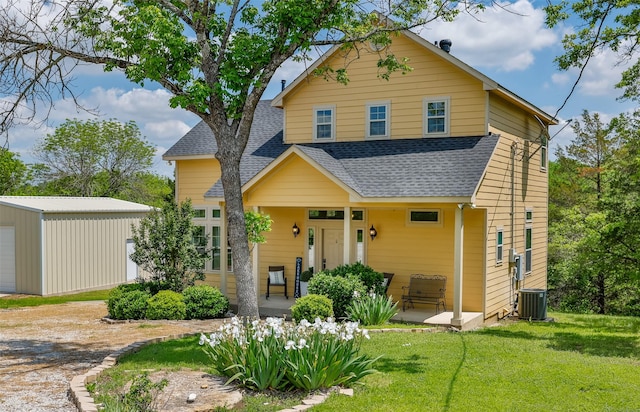 traditional-style house featuring central air condition unit, an outdoor structure, a porch, a front yard, and roof with shingles