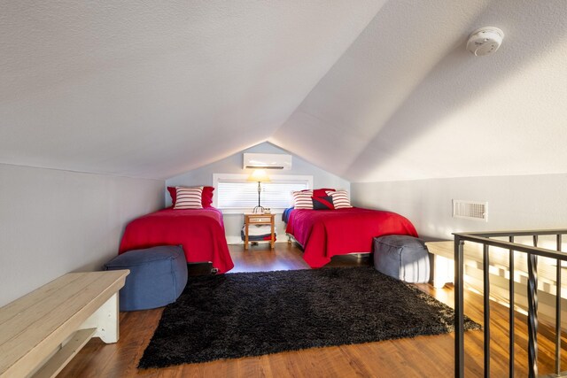 bedroom featuring wood finished floors, visible vents, vaulted ceiling, and a wall unit AC