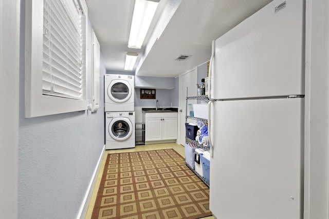 laundry room featuring a sink, cabinet space, baseboards, stacked washer and dryer, and visible vents