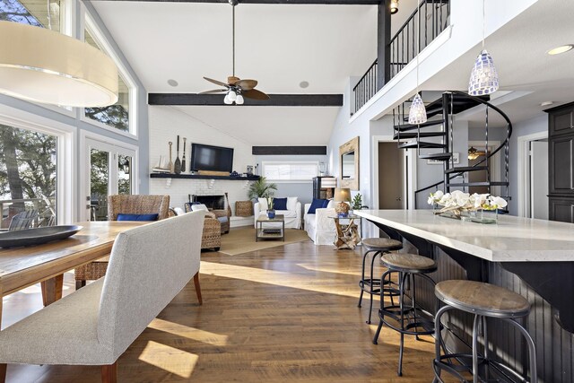 dining space with dark wood-style floors, beamed ceiling, a brick fireplace, stairs, and ceiling fan