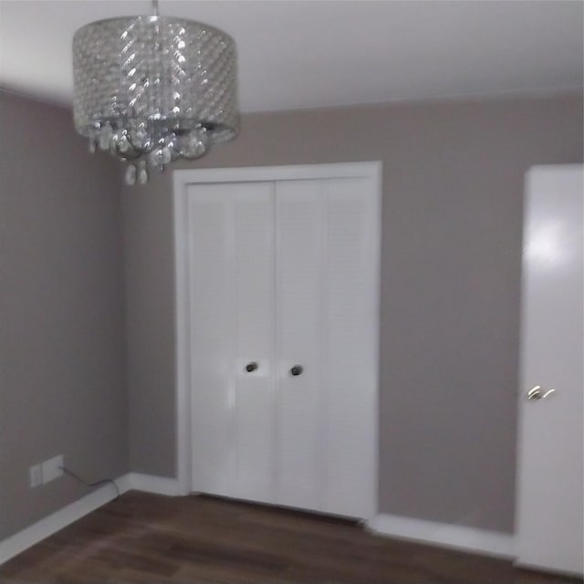 unfurnished bedroom with a chandelier, wood finished floors, a closet, and baseboards