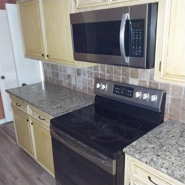 kitchen with range with electric stovetop, dark wood-style floors, stainless steel microwave, tasteful backsplash, and cream cabinets