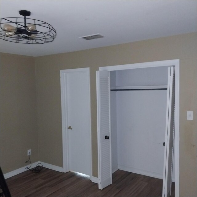 unfurnished bedroom with baseboards, visible vents, dark wood-type flooring, and a closet